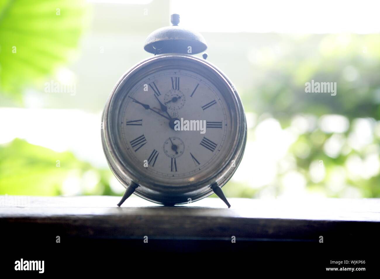 Old alarm bell clock at the window backlit in a house room with plants