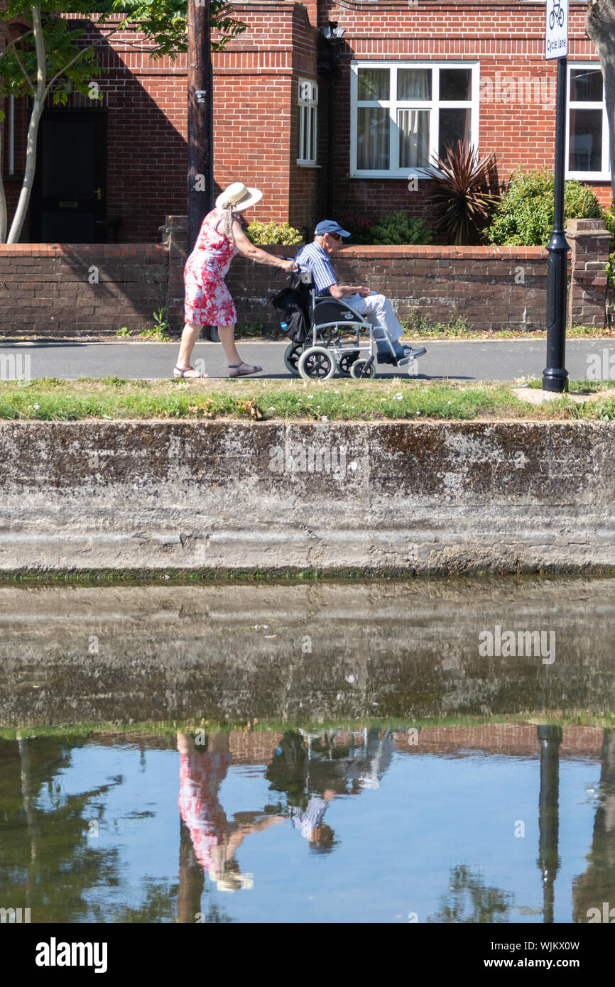 A middle aged woman pushing an elderly man in a wheelchair Stock Photo