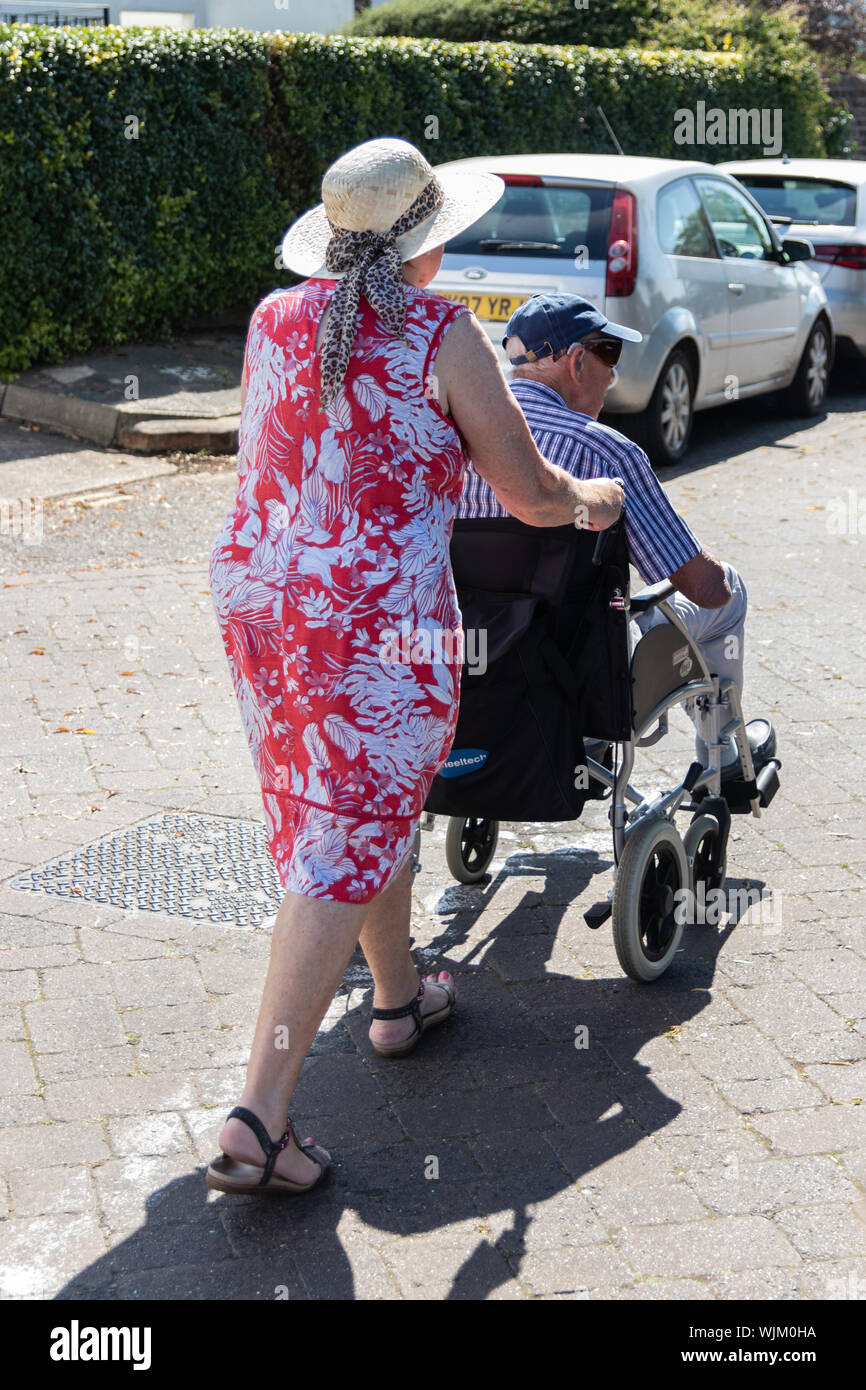 A middle aged woman pushing an elderly man in a wheelchair, Older/disabled person with carer Stock Photo