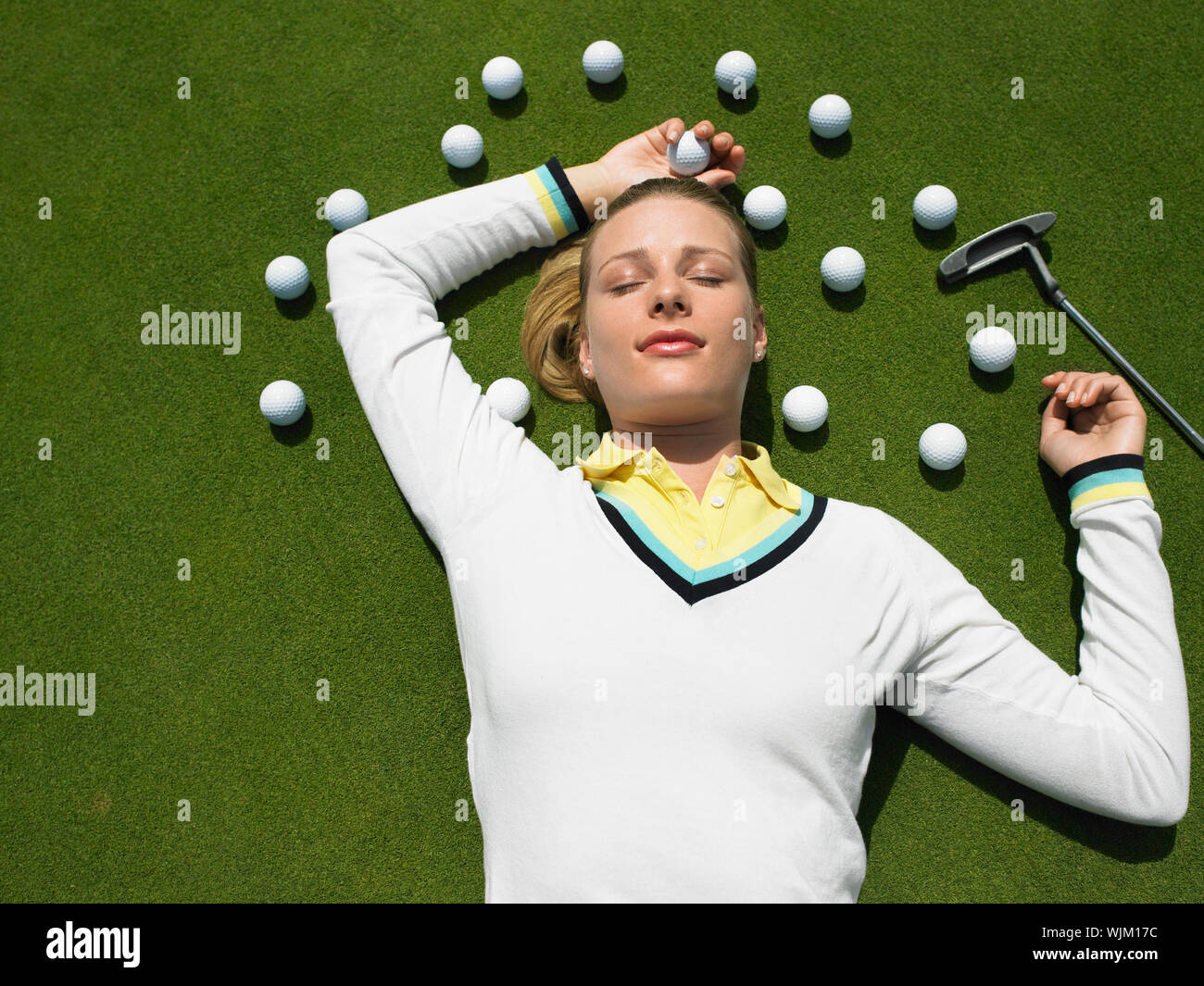 Beautiful female golfer lying on putting green with golf balls and club Stock Photo