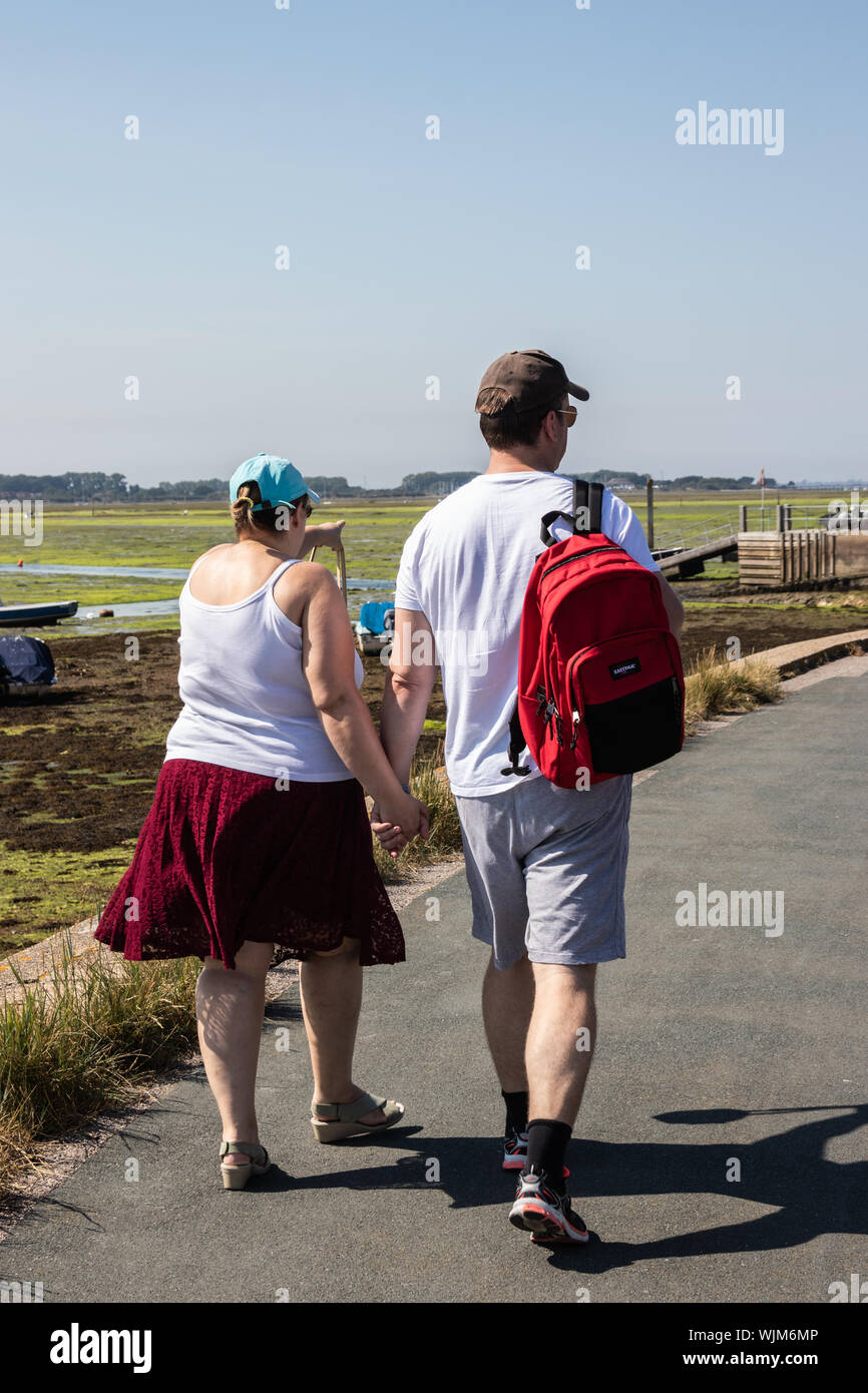 A middle aged couple holding hands walking along a shoreline in summer Stock Photo