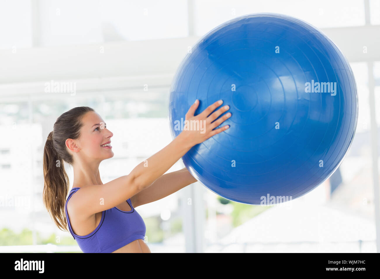 Side view of a smiling fit young woman holding fitness ball in a gym ...