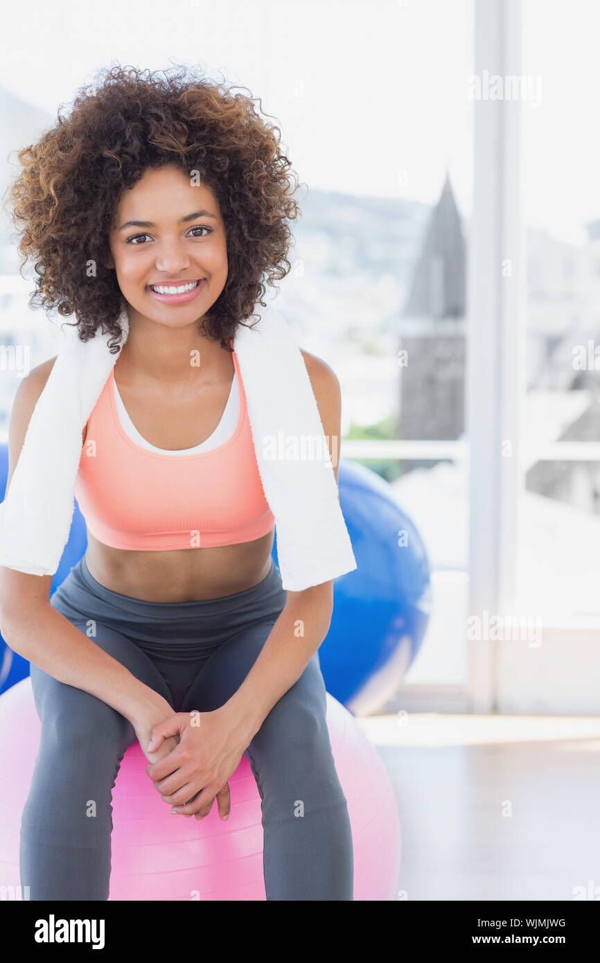 Portrait of a fit young woman sitting on fitness ball at a bright gym ...