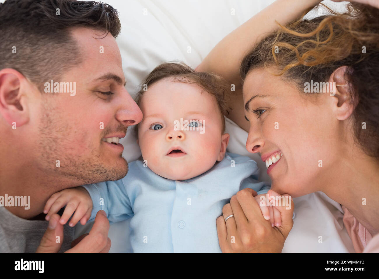 Portrait of cute baby boy with parents in bed Stock Photo Alamy
