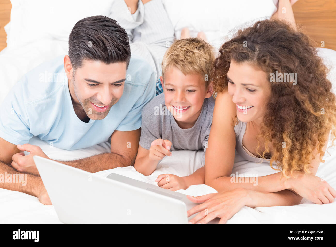 Smiling young family using laptop together on bed at home in bedroom ...