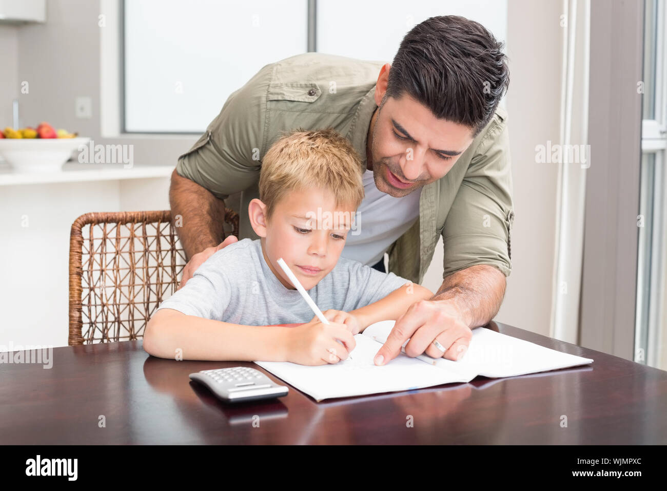 Happy father helping son with math homework at table at home in kitchen ...