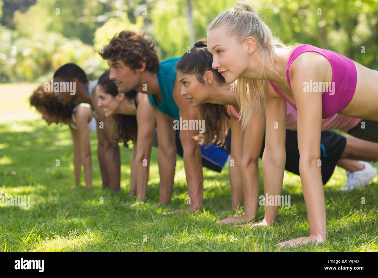 Side view of a group of fitness people doing push ups in the park Stock Photo