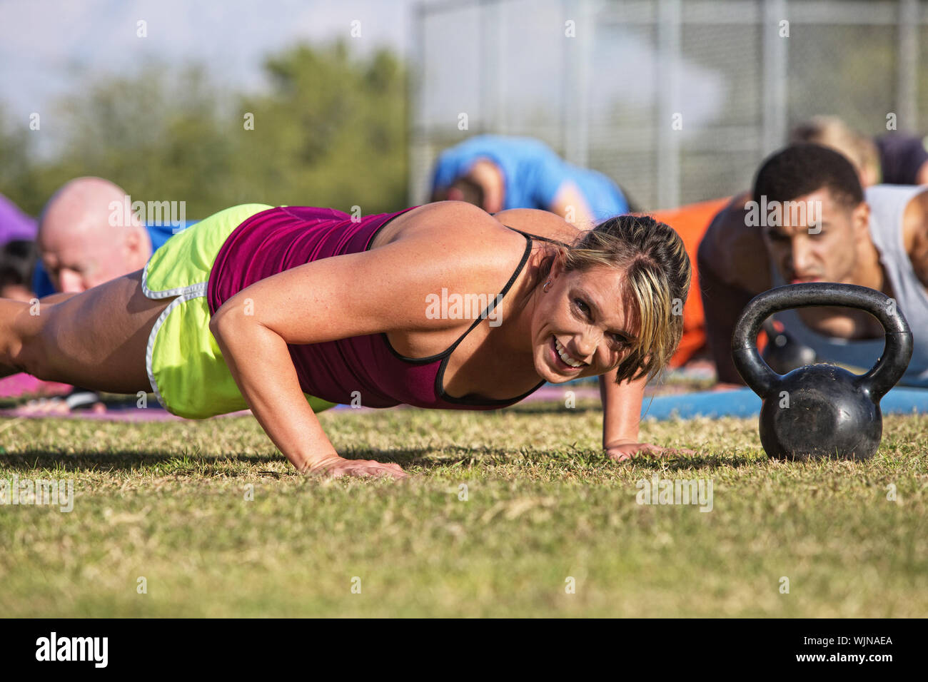Embarrassed woman doing push-ups with group outdoors Stock Photo