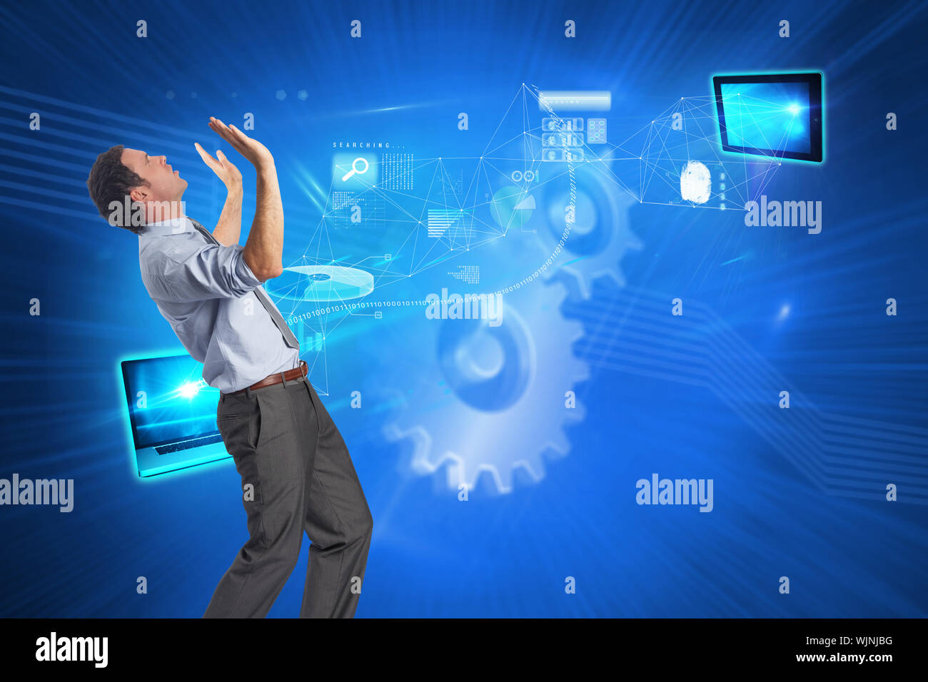 Businessman posing with arms raised against shiny cogs on blue background Stock Photo