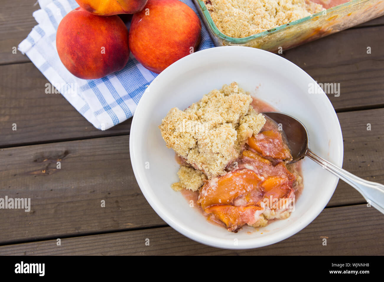 Fresh homemade peach crumble served in a white bowl on an outdoor picnic  table during the summer Stock Photo