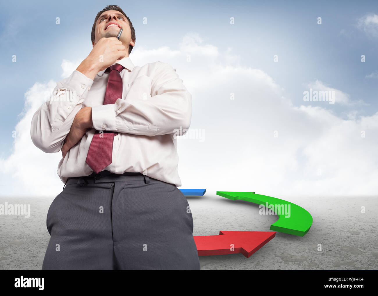 Thoughtful businessman holding pen to chin against blue red and green arrows in desert landscape Stock Photo