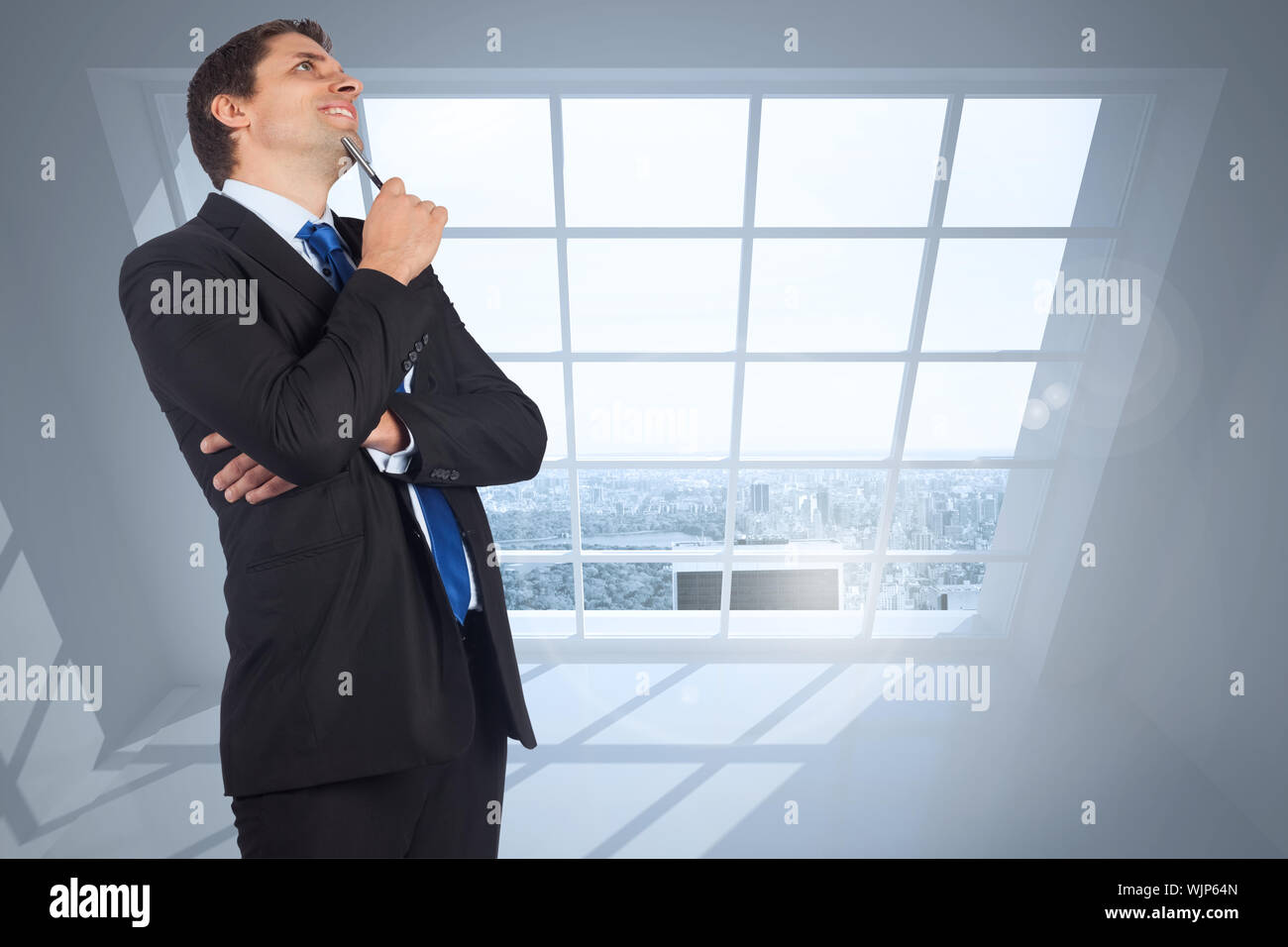 Thinking businessman holding pen against room with large windows ...