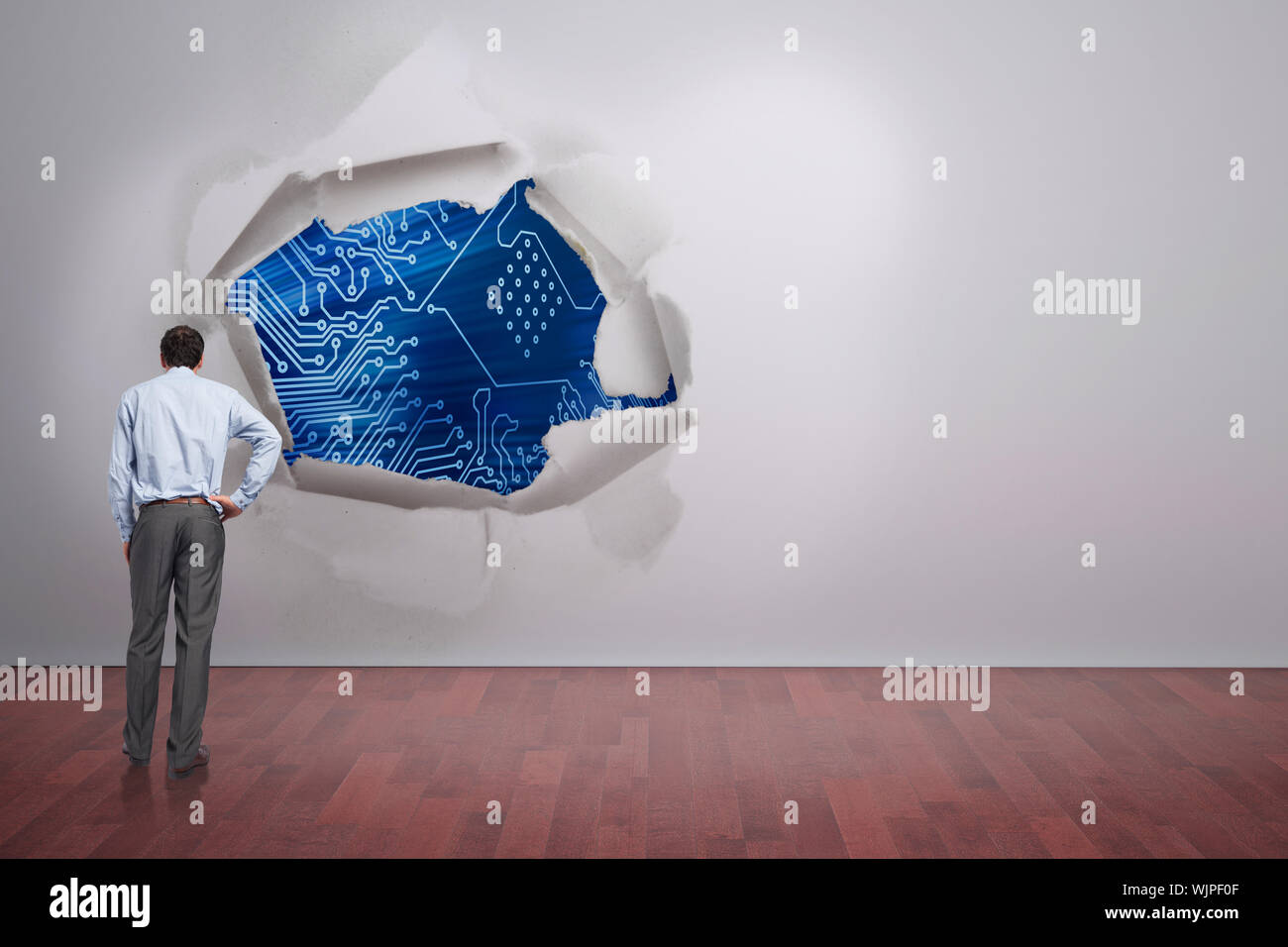 Businessman with hand on hip against rip on wall showing circuit board ...