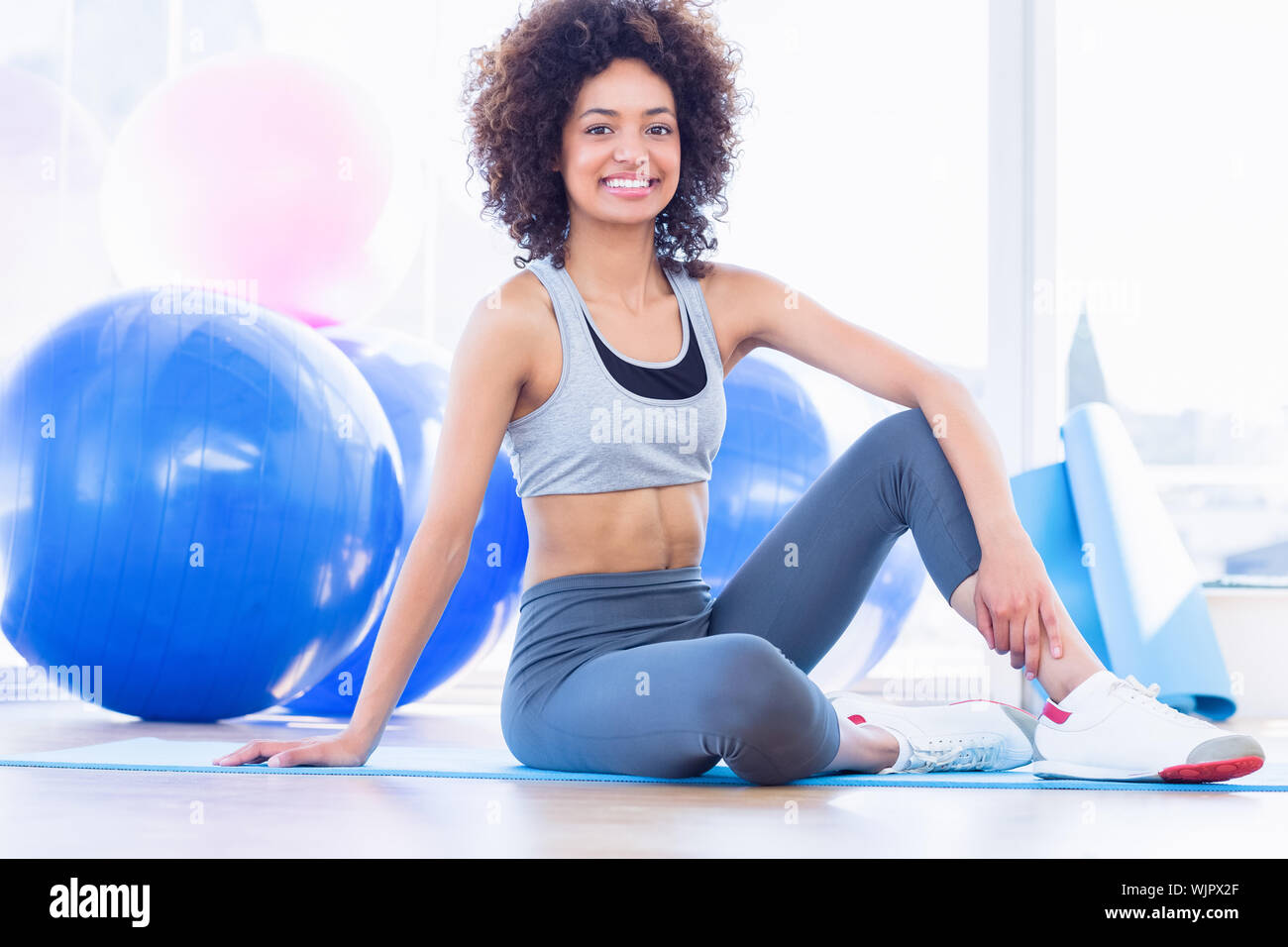 Full length portrait of a fit young woman sitting on exercise mat in a ...
