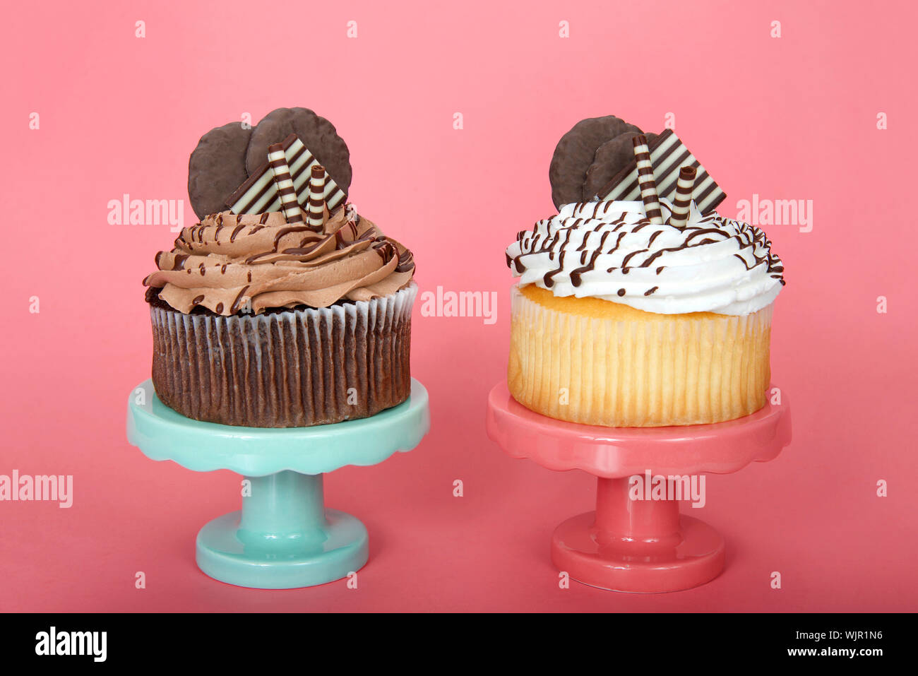 Giant vanilla an chocolate cup cakes with vanilla frosting embellished with white and dark chocolate wafers and cookies on a pink and green pedestals Stock Photo
