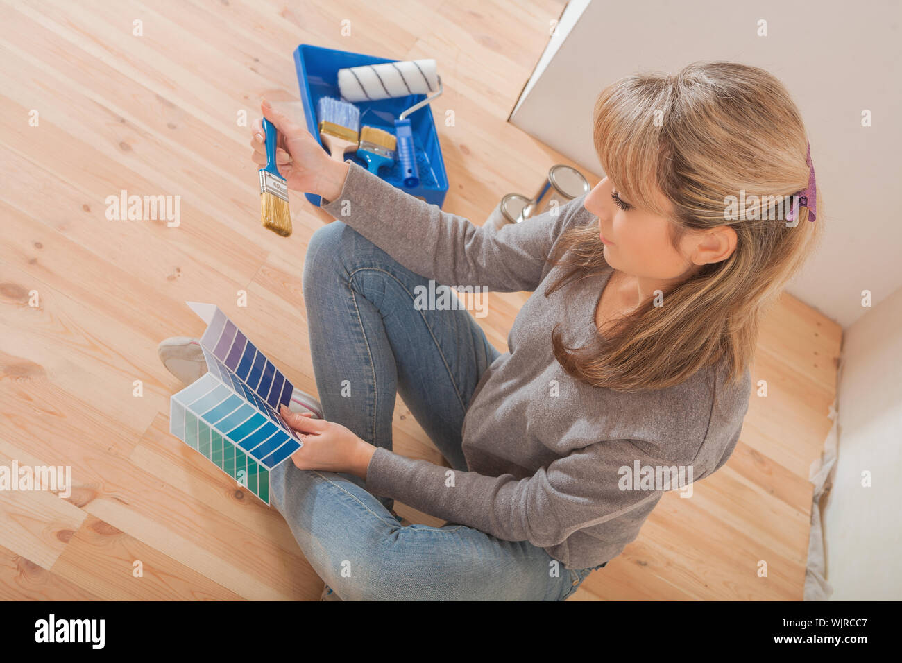 female holding color palette and paintbrush and sitting on wooden floor ...