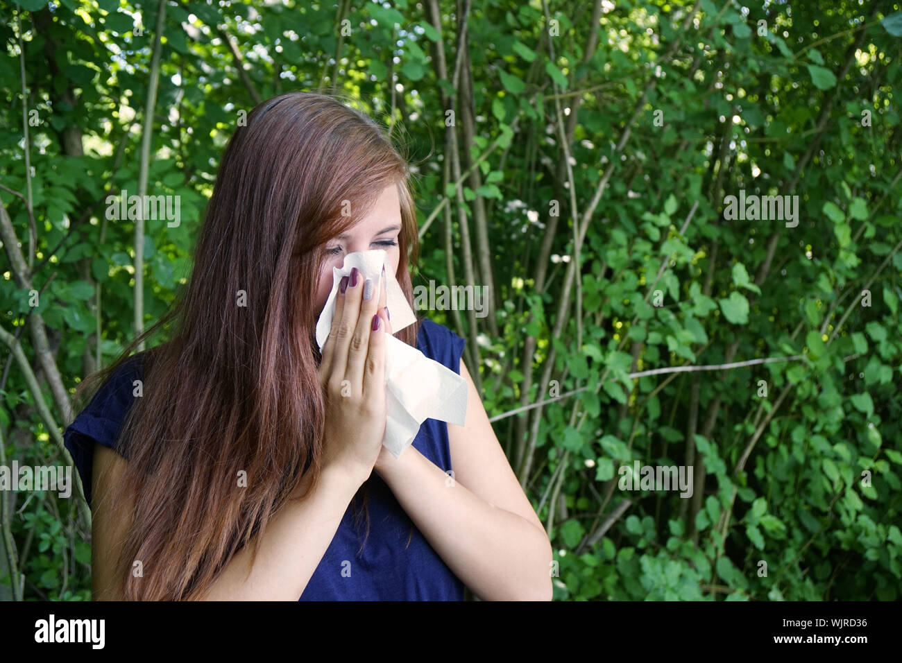 Young Woman By Plants Blowing Nose Stock Photo