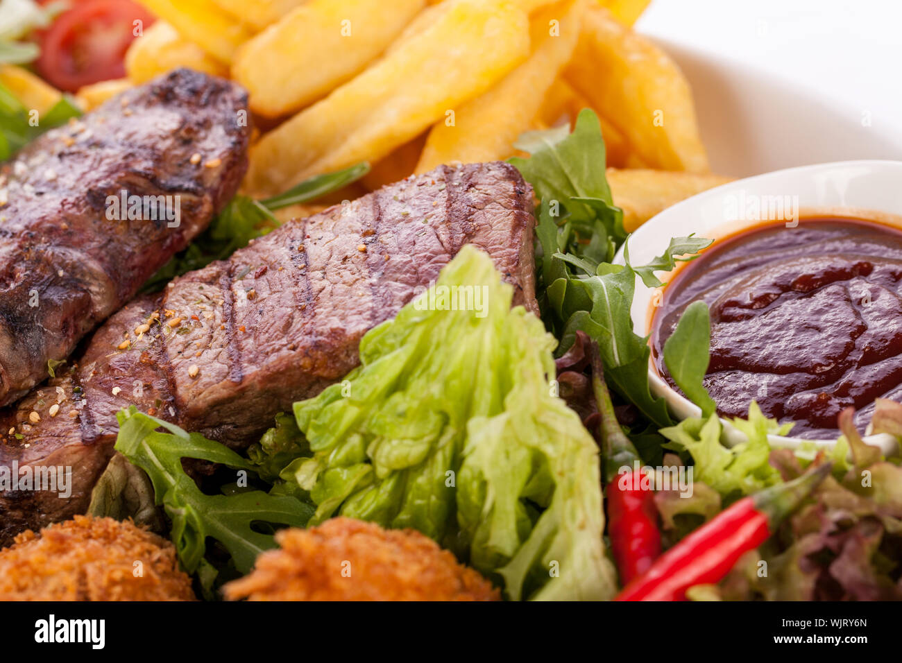 Wholesome platter of mixed meats including grilled steak, crispy crumbed chicken and beef on a bed of fresh leafy green mixed salad served with French Stock Photo