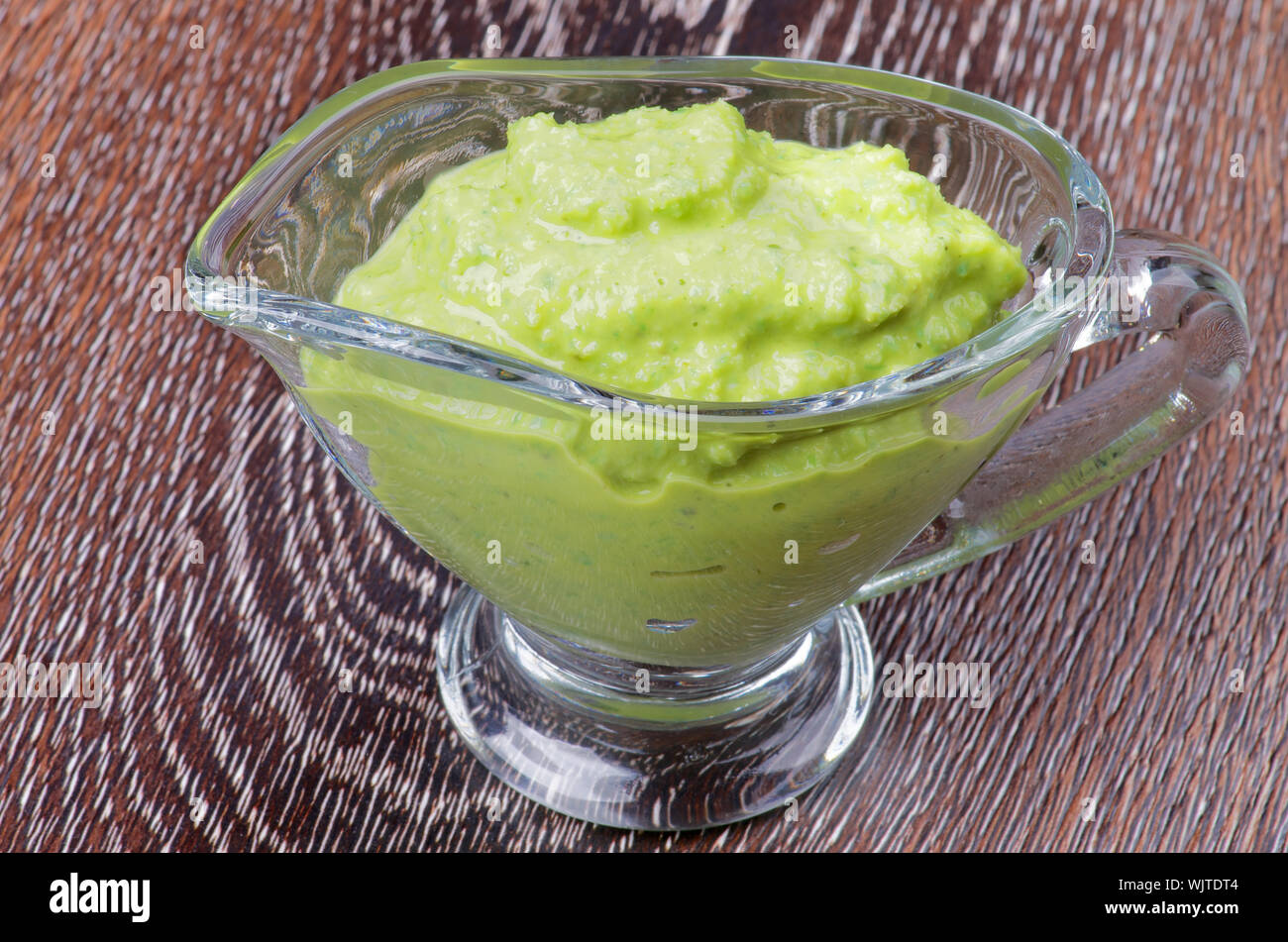Hot Wasabi Sauce in Glass Gravy Boat isolated on Wooden background Stock Photo