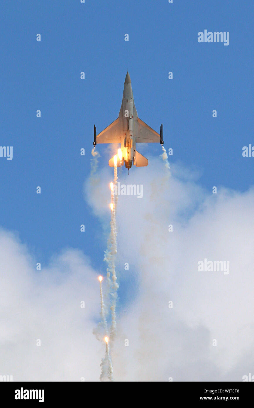 A General Dynamics F-16 Fighting Falcon of the Belgian Air Force climbs vertically and drops flares as it leaves the clouds for the clear blue sky. Stock Photo