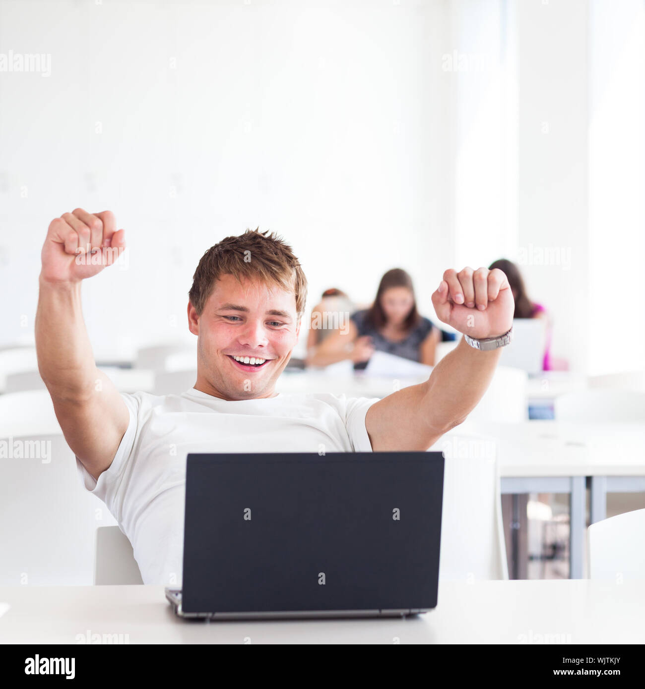 Portrait of a very happy young, male college student working on his laptop computer in a classroom/study room/library - expressing joy/success (shallo Stock Photo