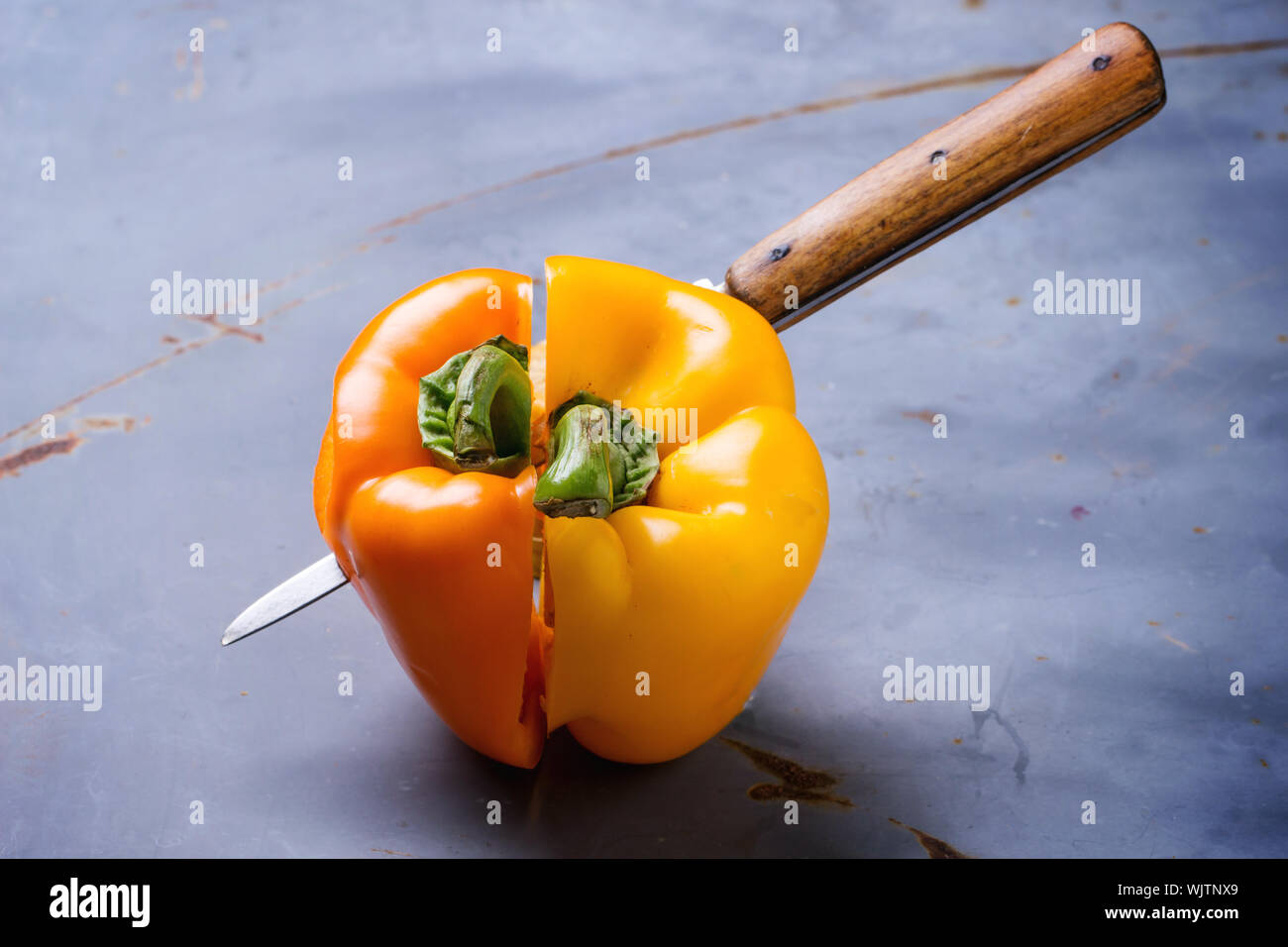 Close-up Of Knife With Yellow And Orange Halved Bell Peppers On Table Stock Photo