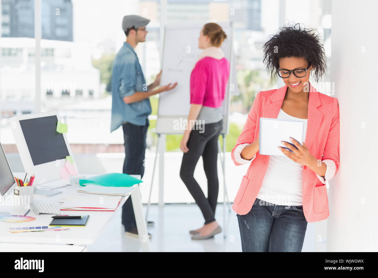 Casual female artist using digital tablet with colleagues in the background at a bright office Stock Photo