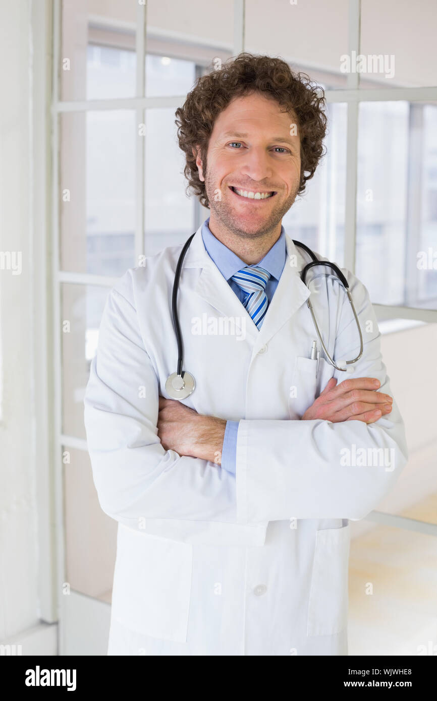 Portrait of a happy handsome male doctor standing with arms crossed in ...