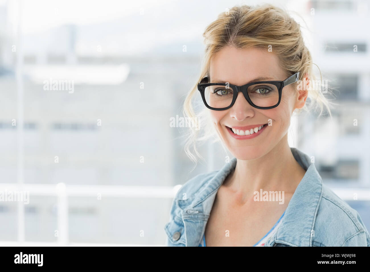 Pretty blonde designer smiling at camera in creative office Stock Photo