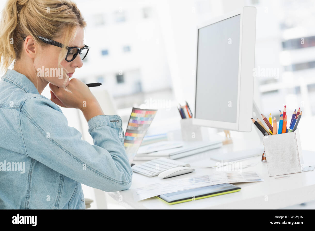 Blonde focused designer working at her desk in creative office Stock Photo