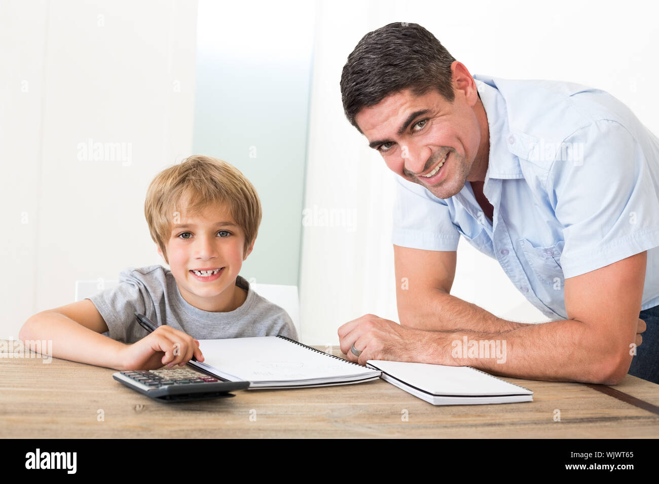Portrait of happy father assisting son with homework at table in house Stock Photo