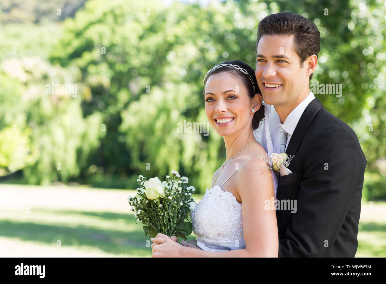 Happy loving newly wed couple looking away while standing in park Stock Photo