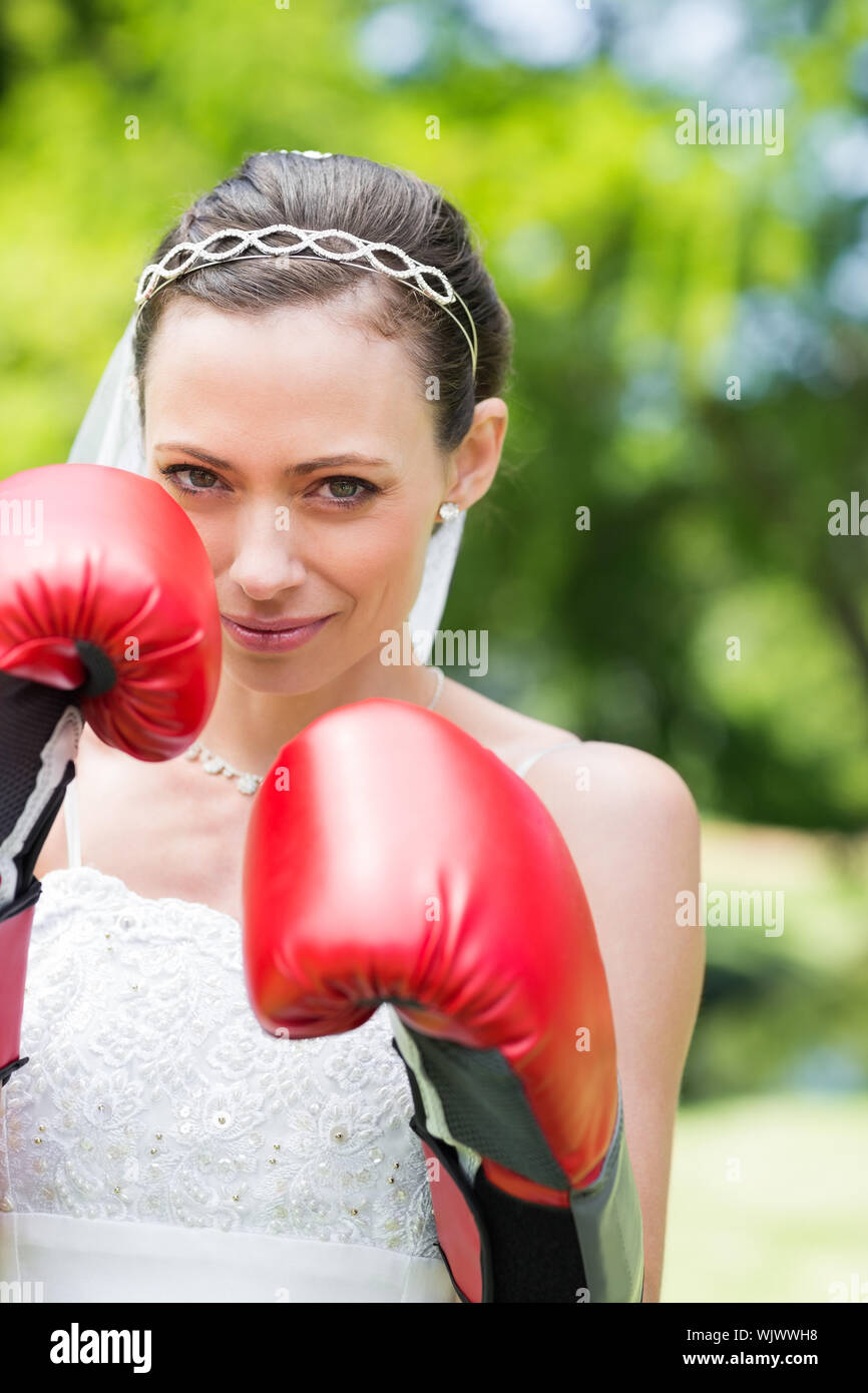 Portrait of woman in wedding dress wearing boxing gloves in park Stock