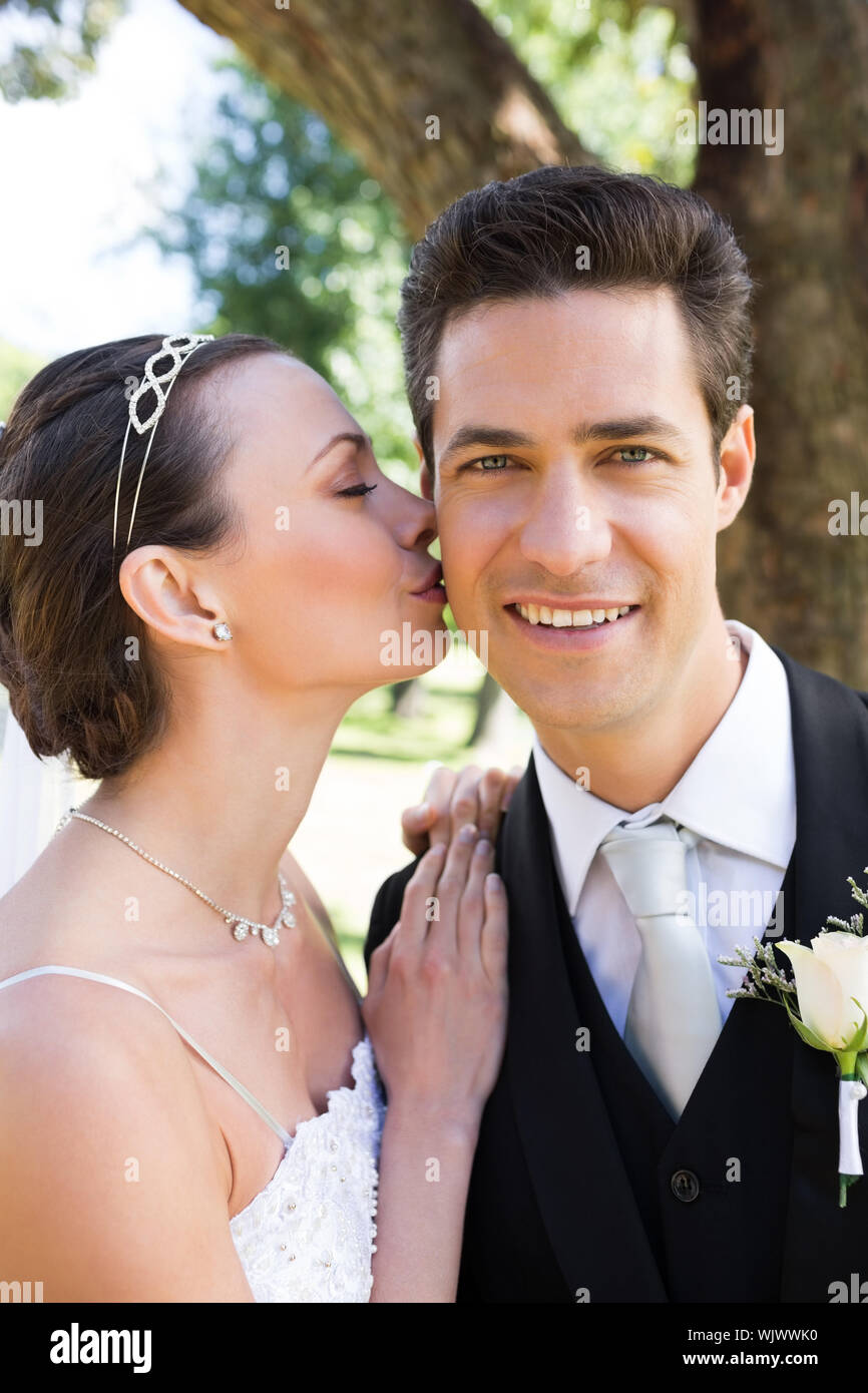 Beautiful young bride kissing happy groom on cheek in garden Stock ...