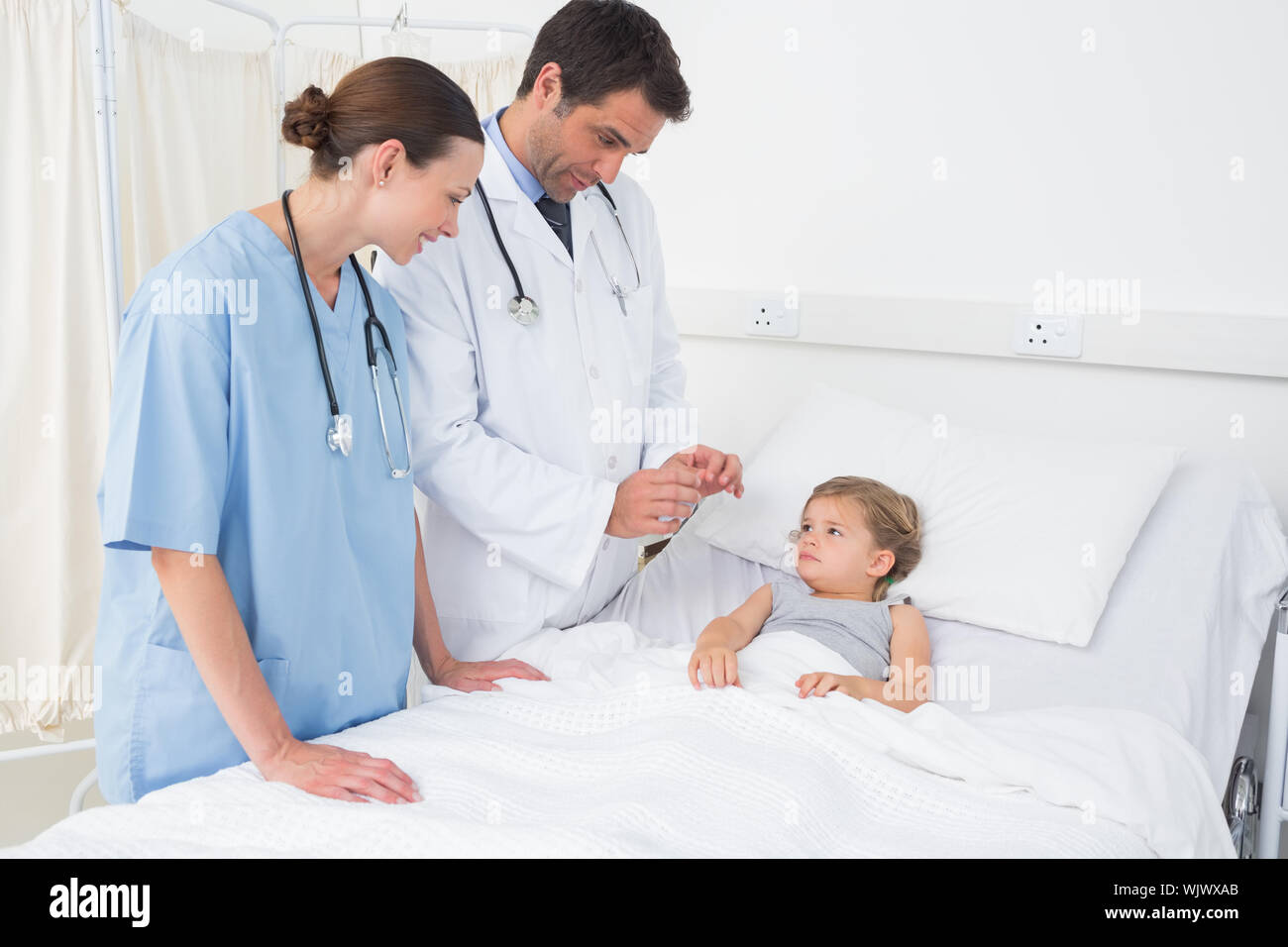 Doctors attending little girl lying in hospital bed Stock Photo