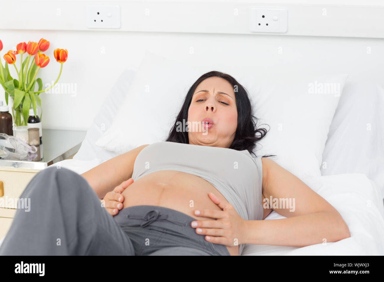 Pregnant woman suffering from labor pains lying in bed at hospital Stock Photo