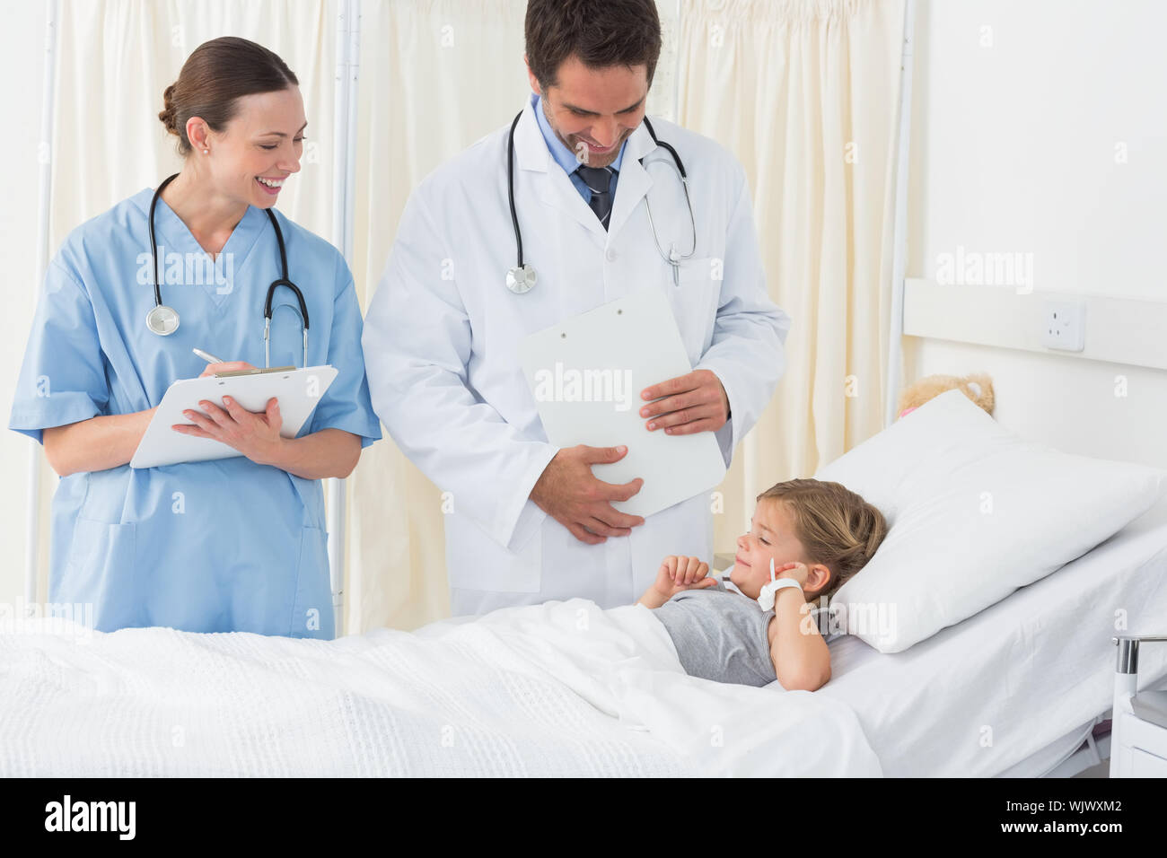 Smiling doctors attending sick girl lying in hospital bed Stock Photo
