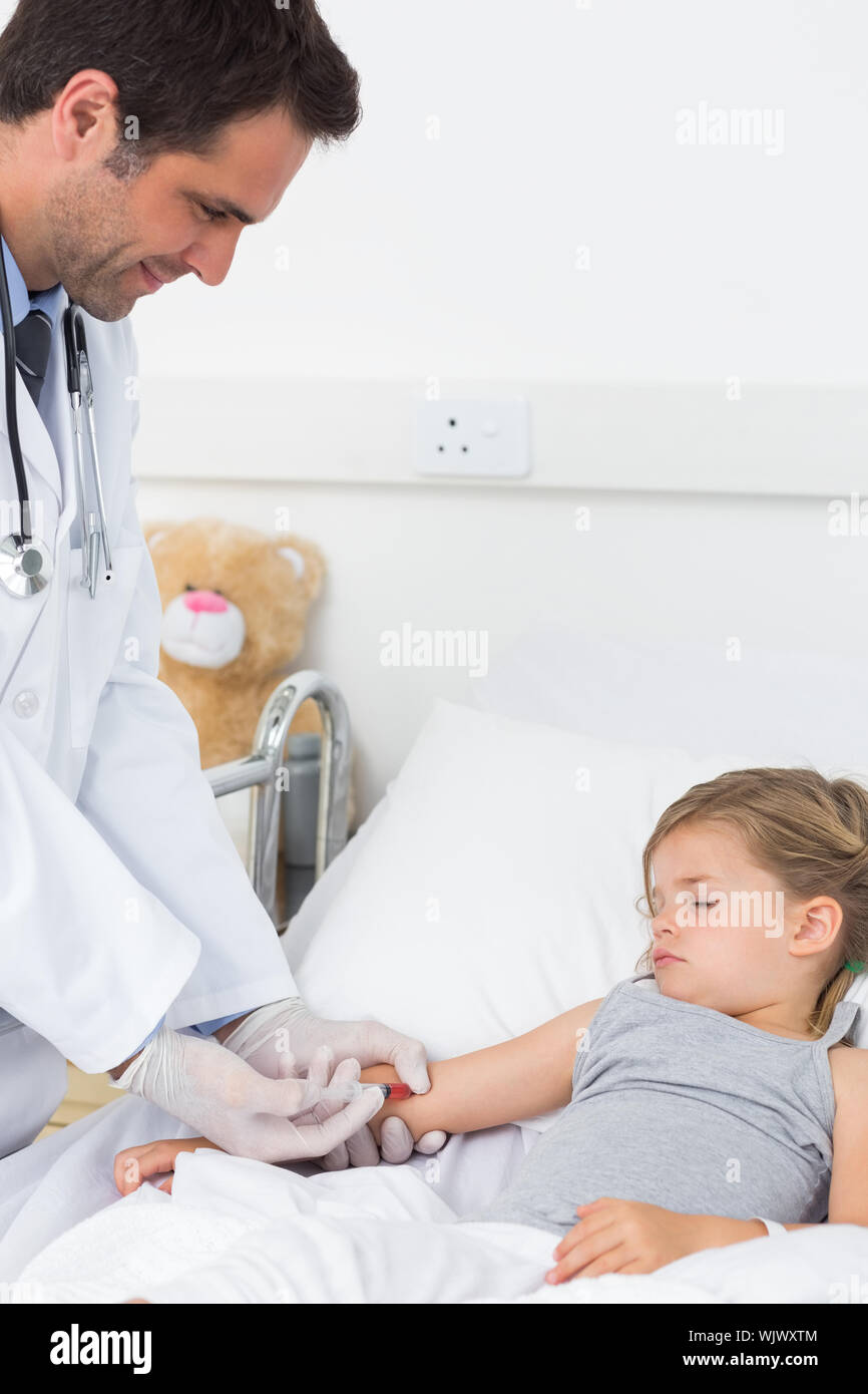 Male doctor giving injection to ill girl lying in hospital bed Stock Photo