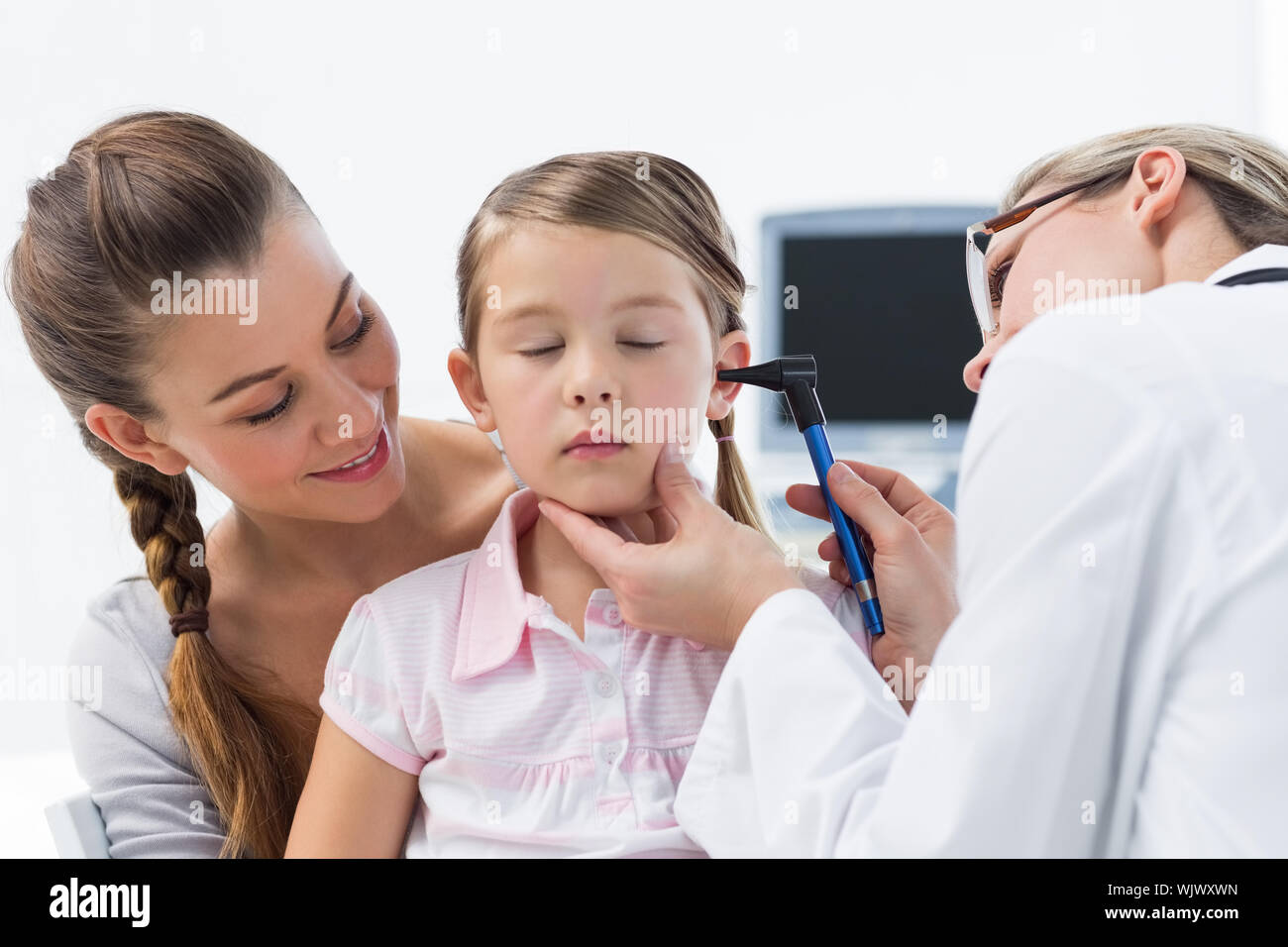 Mother with girl being examined by female doctor with otoscope Stock Photo