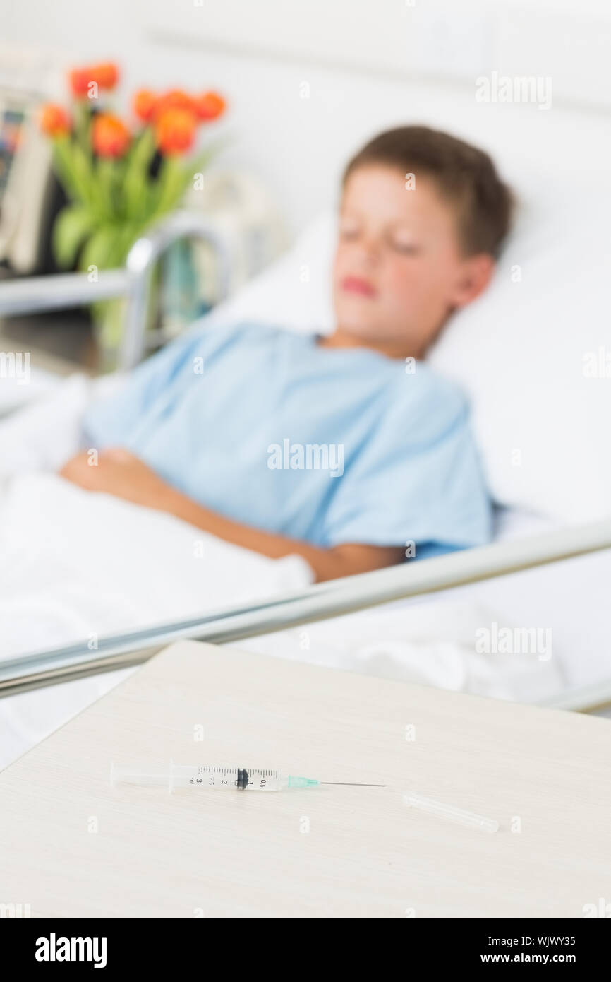 Focus on syringe on table with boy resting in hospital ward Stock Photo