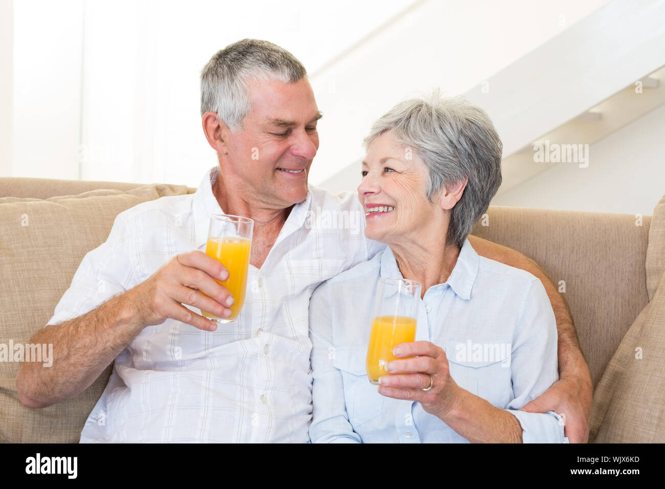 Senior couple sitting on couch drinking orange juice at home in living ...