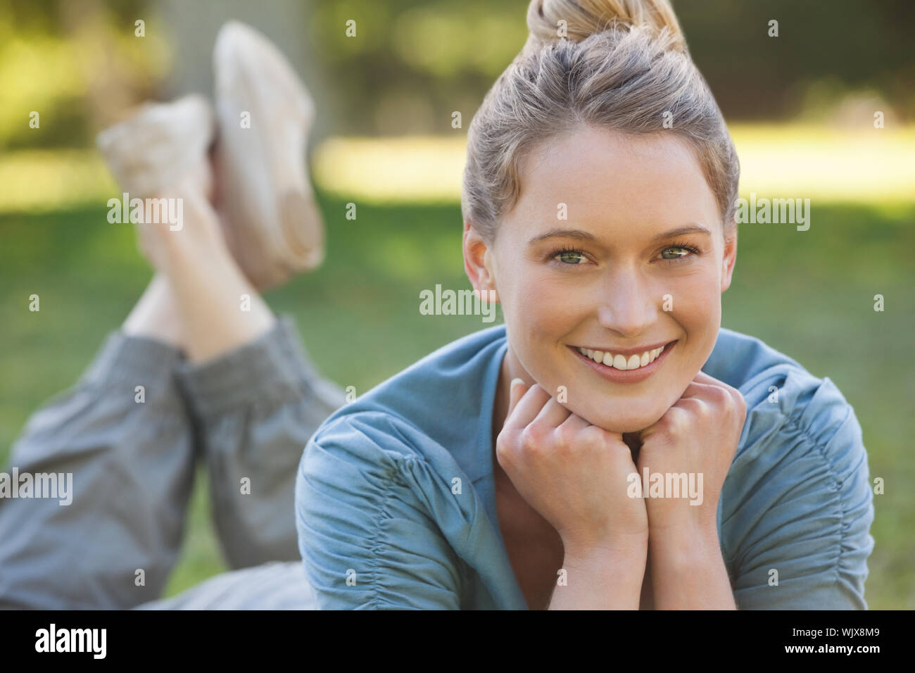 Portrait of a beautiful relaxed young woman lying on grass at the park ...