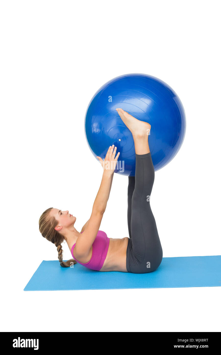 Side view of a fit young woman exercising with fitness ball over white ...