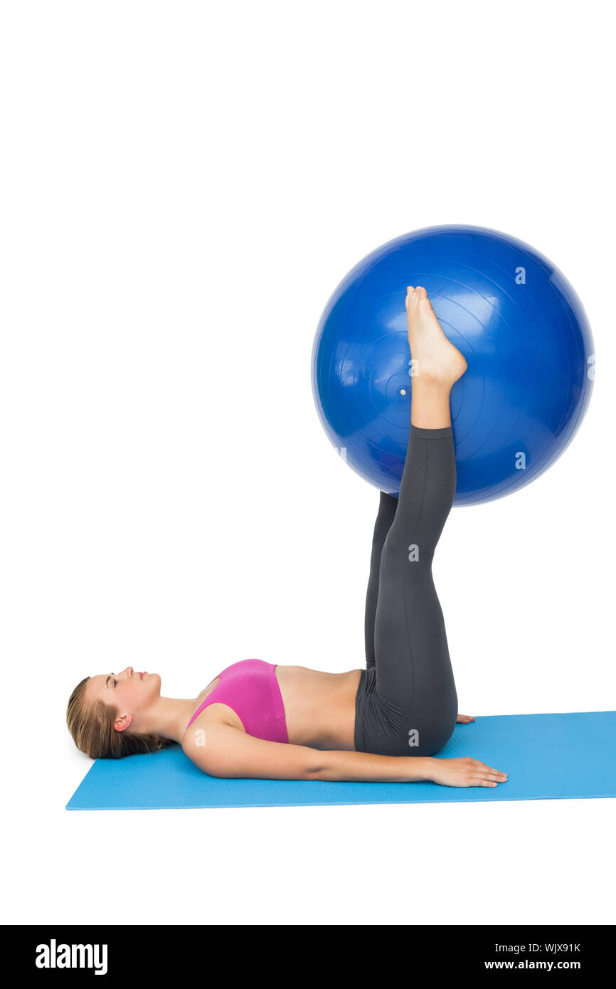 Side view of a fit young woman exercising with fitness ball over white ...