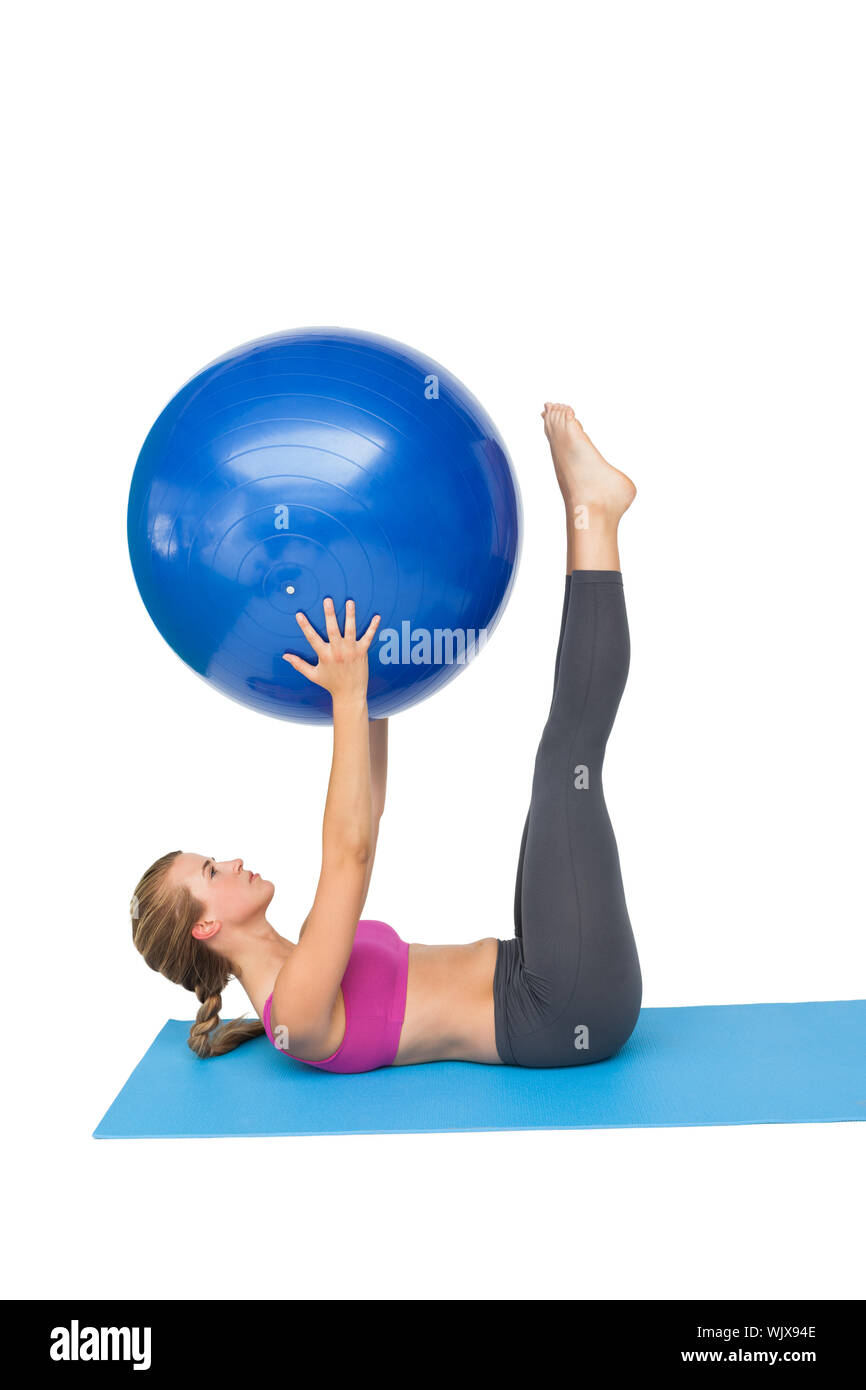 Side view of a fit young woman exercising with fitness ball over white ...