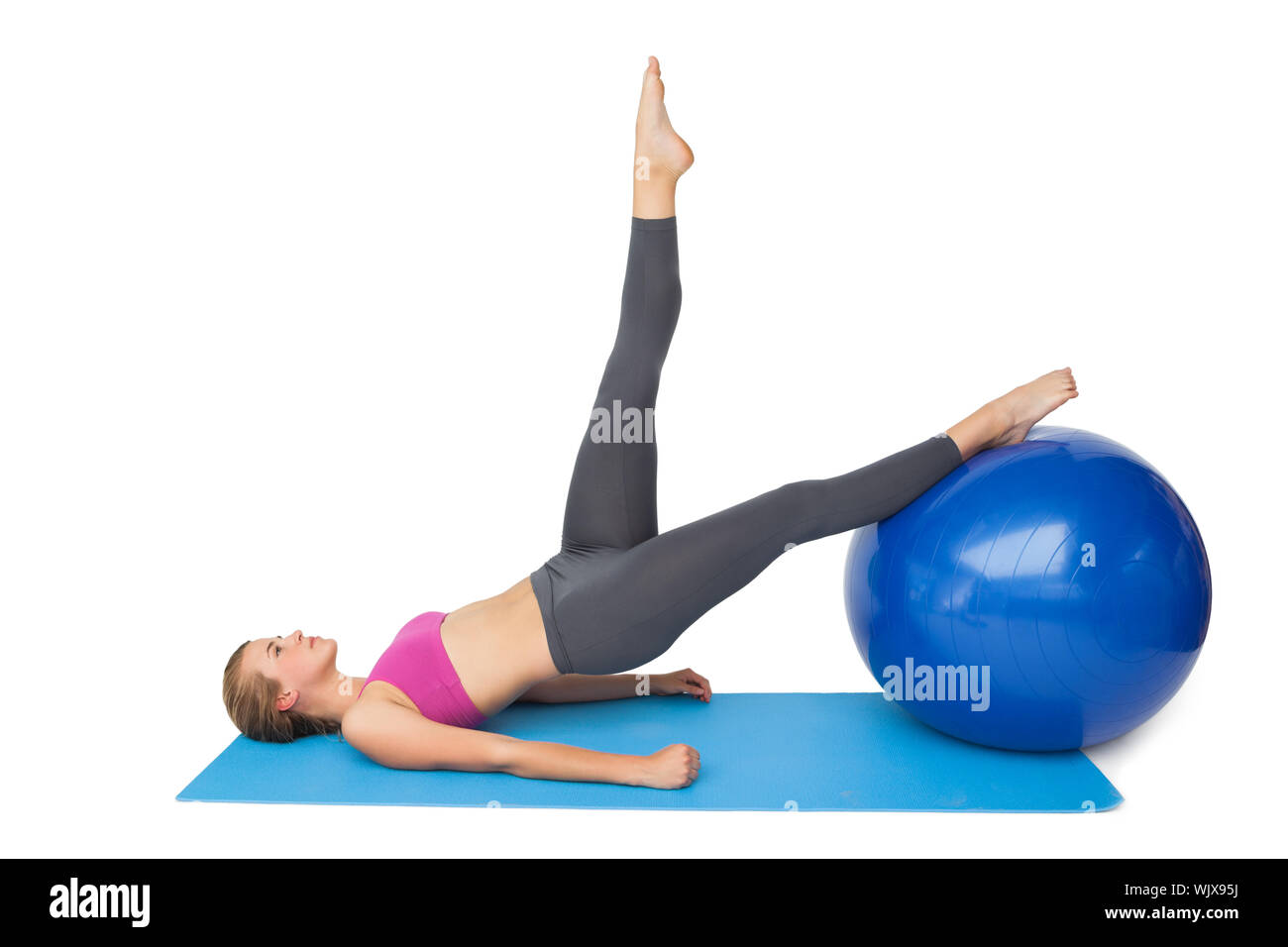 Side view of a fit young woman exercising with fitness ball over white ...