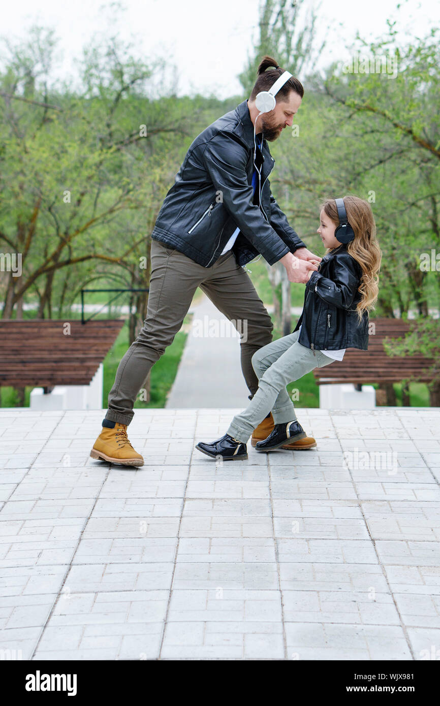 Happy little girl dances with young father in middle city street. Happy family time. Father and daughter dancing outdoors. Fashionable stylish family Stock Photo