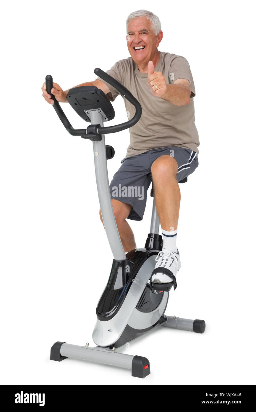 Full length of a senior man gesturing thumbs up on stationary bike over white background Stock Photo