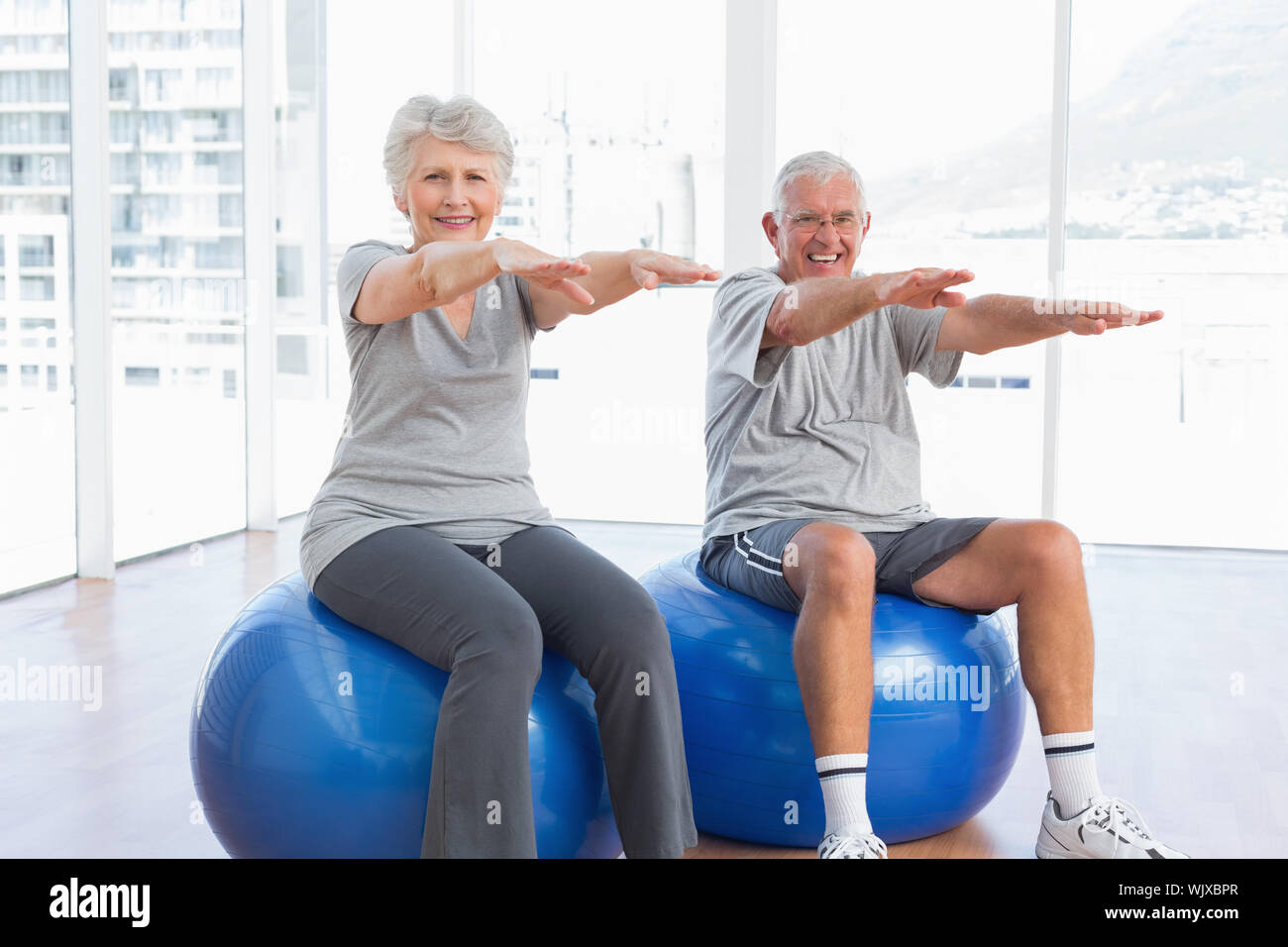 Happy senior couple doing stretching exercises on fitness balls in the