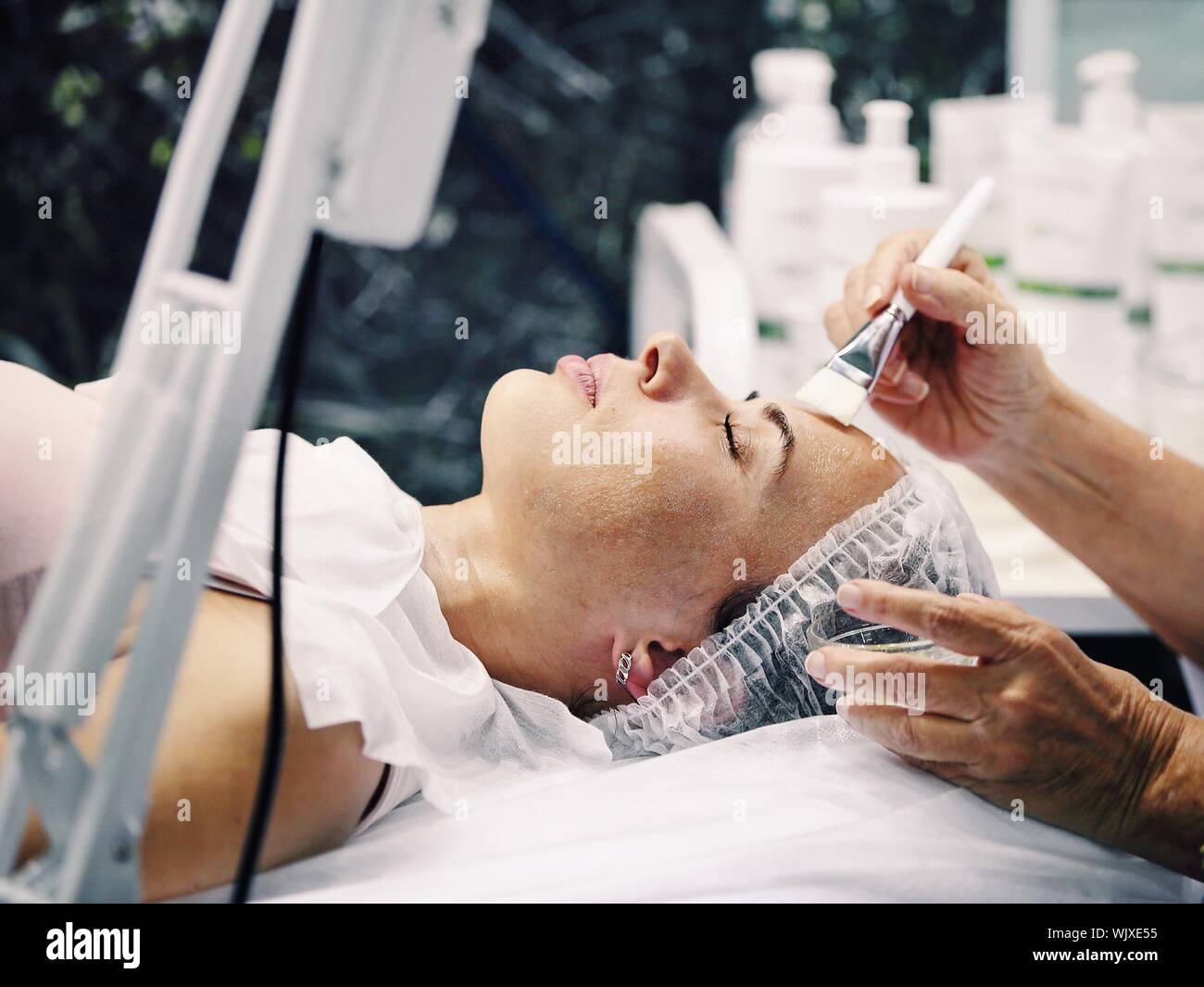 Cropped Hands On Cosmetologist Applying Cream On Female Customer Head Stock Photo
